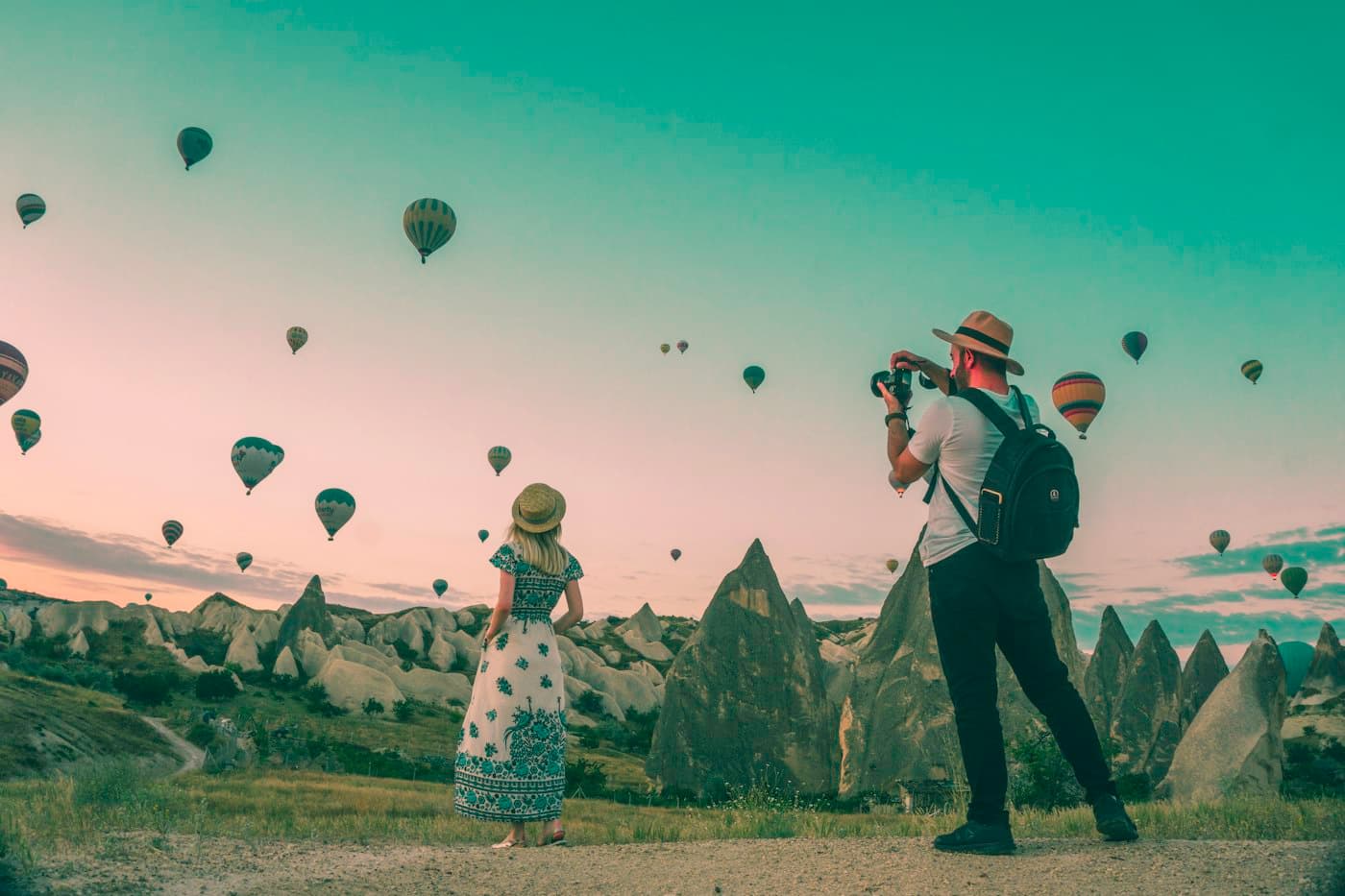 Travellers watching hot-air balloons rise over a valley